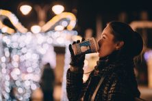 a women drinking coffee outside with christmas lights in the background