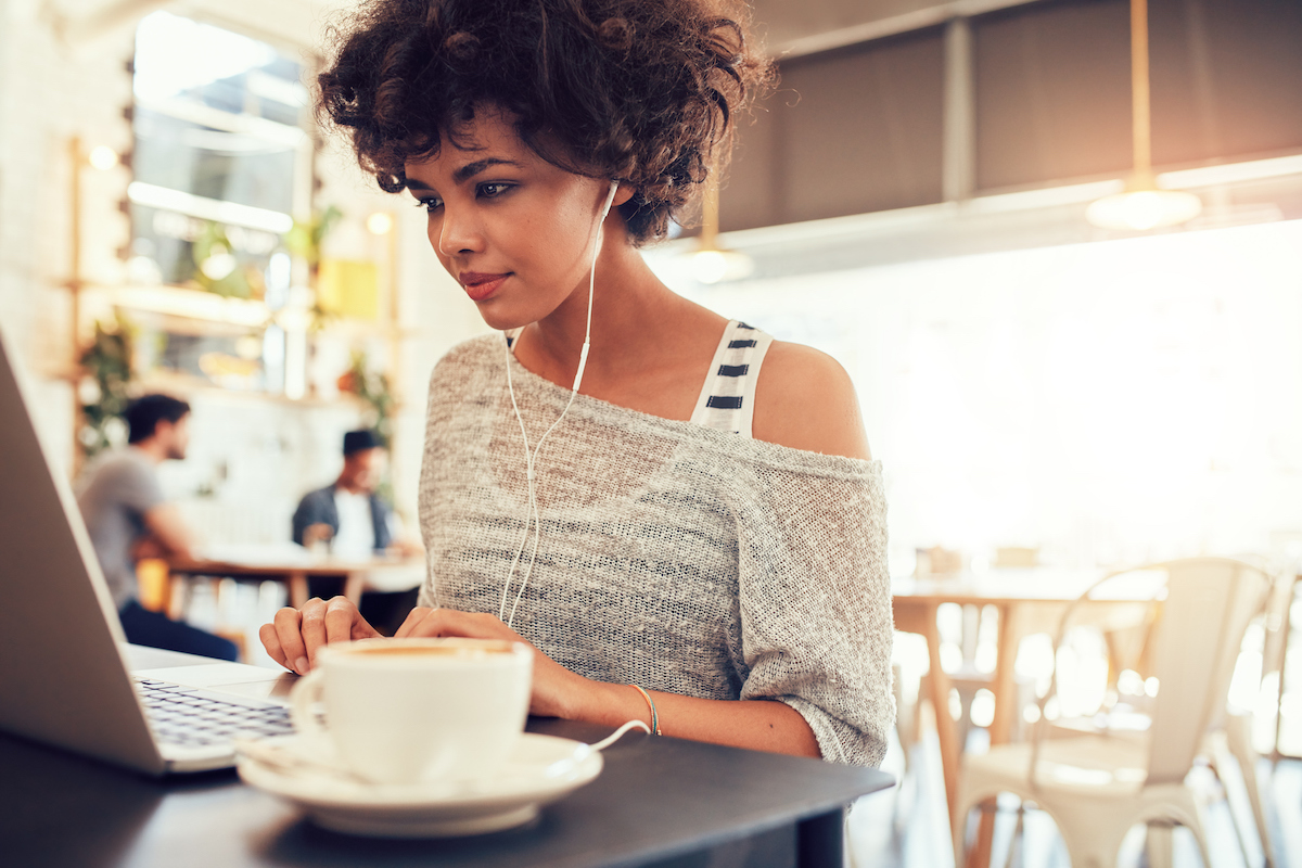 Portrait of a young woman with earphones using laptop at a cafe.