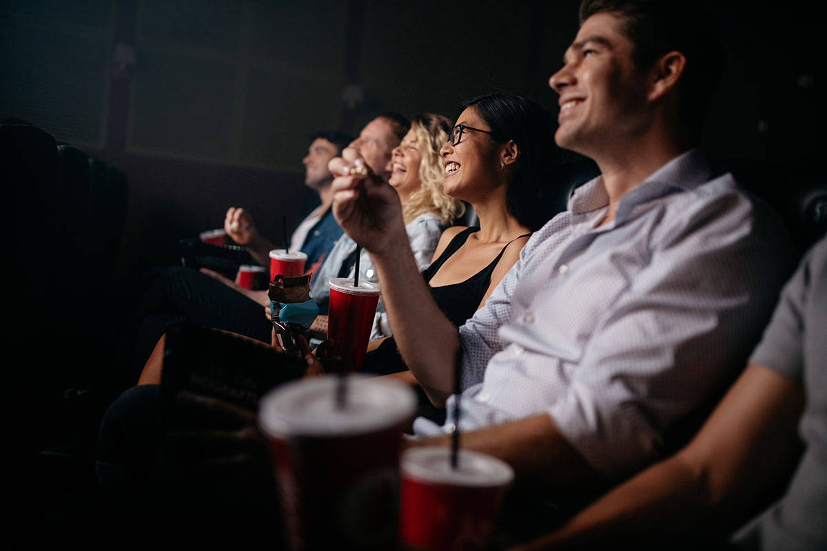 Group of people in theater with popcorn and drinks. Young friends watching movie in cinema.