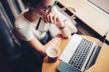 A woman looks at her laptop and holds her credit card at a coffee shop.