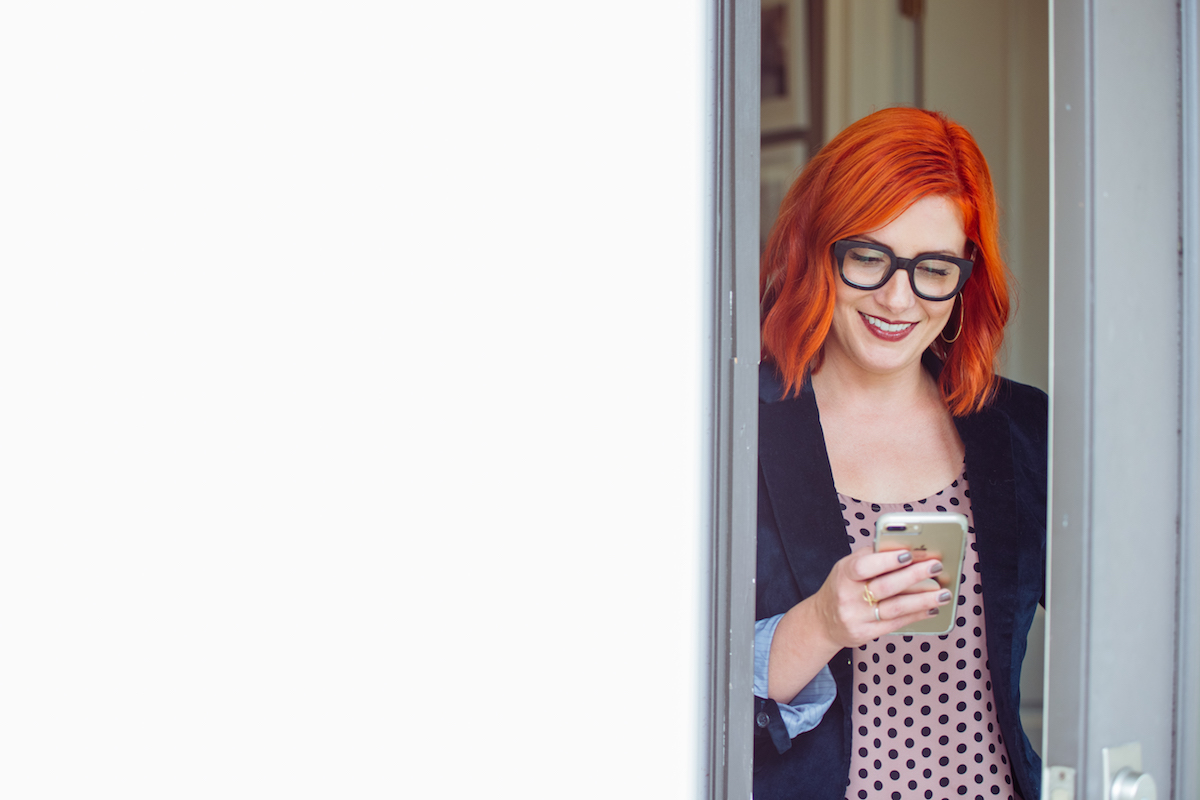 A woman uses her phone as she stands against a doorway.