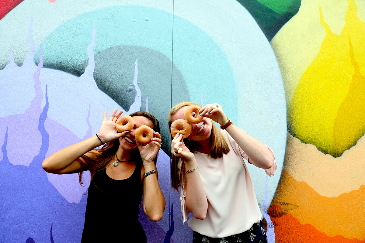 Two girls holding donuts in front of mural