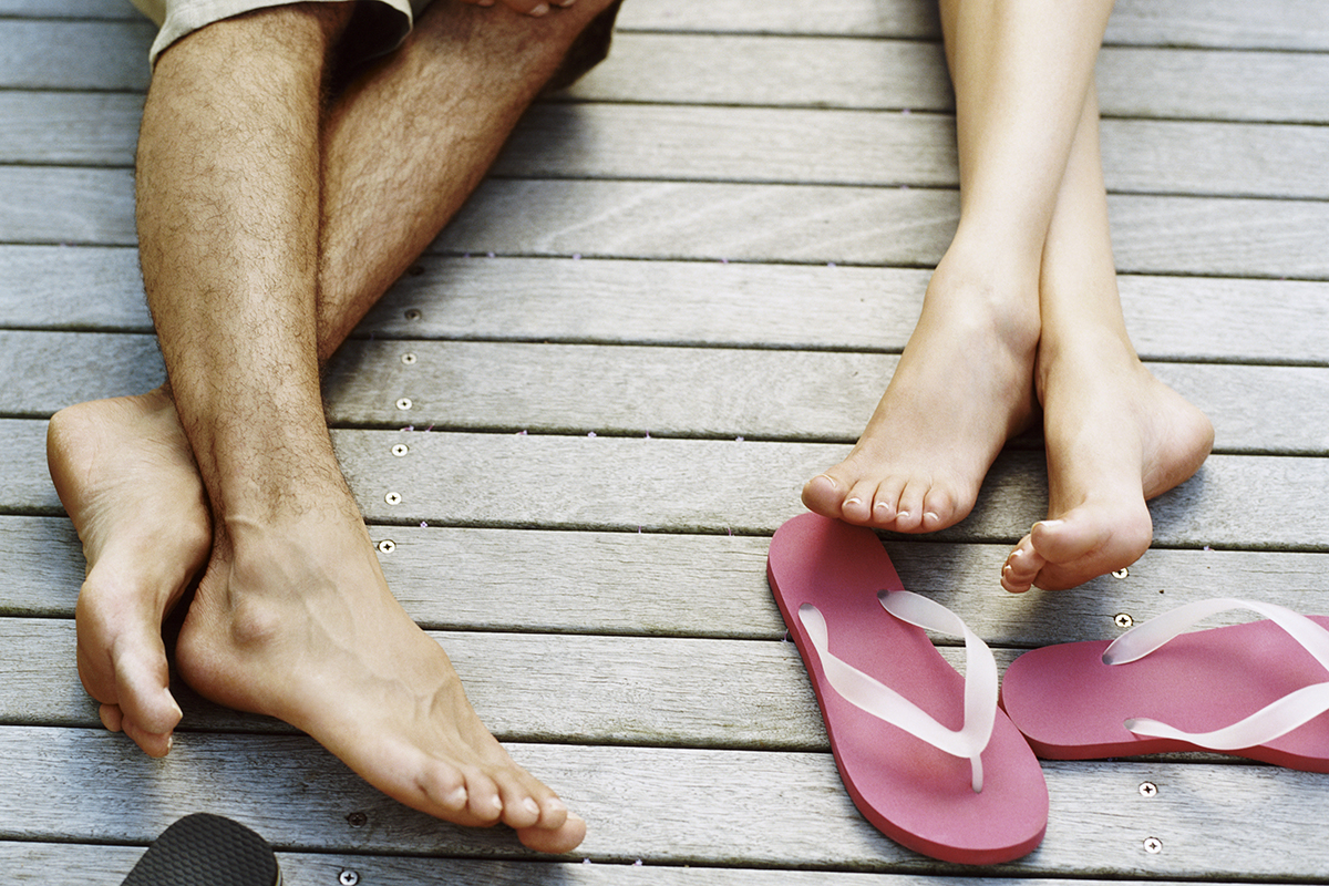 detail of a couple's legs on a wooden deck with flip flops.