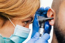 An ear, nose, and throat specialist examines a patient&rsquo;s right ear canal with an otoscope.