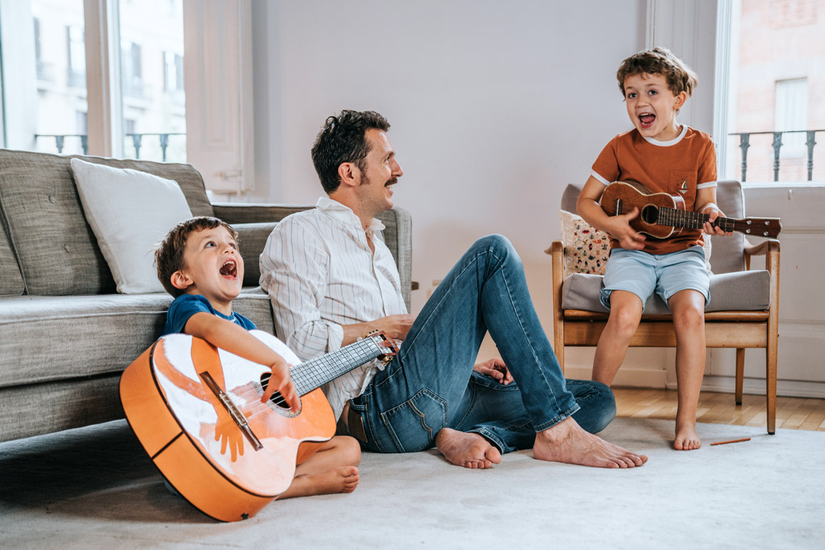 Two children play guitar for their father. 