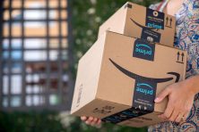 A woman carries a stack of amazon boxes