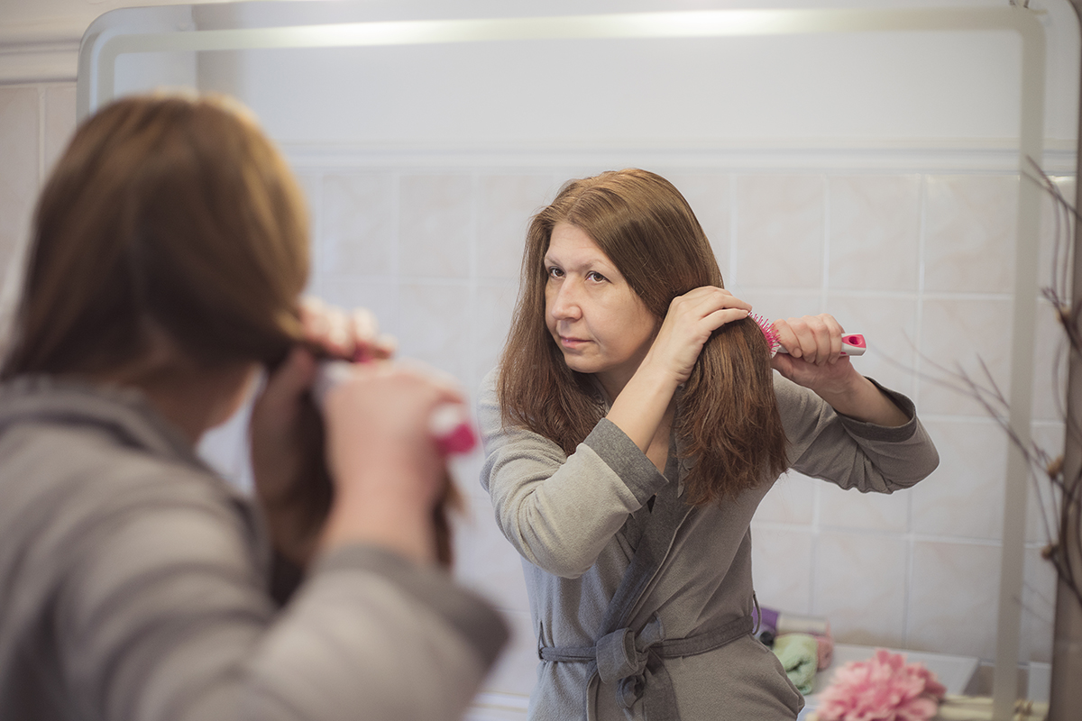 A woman brushes her hair in her bathroom at home.