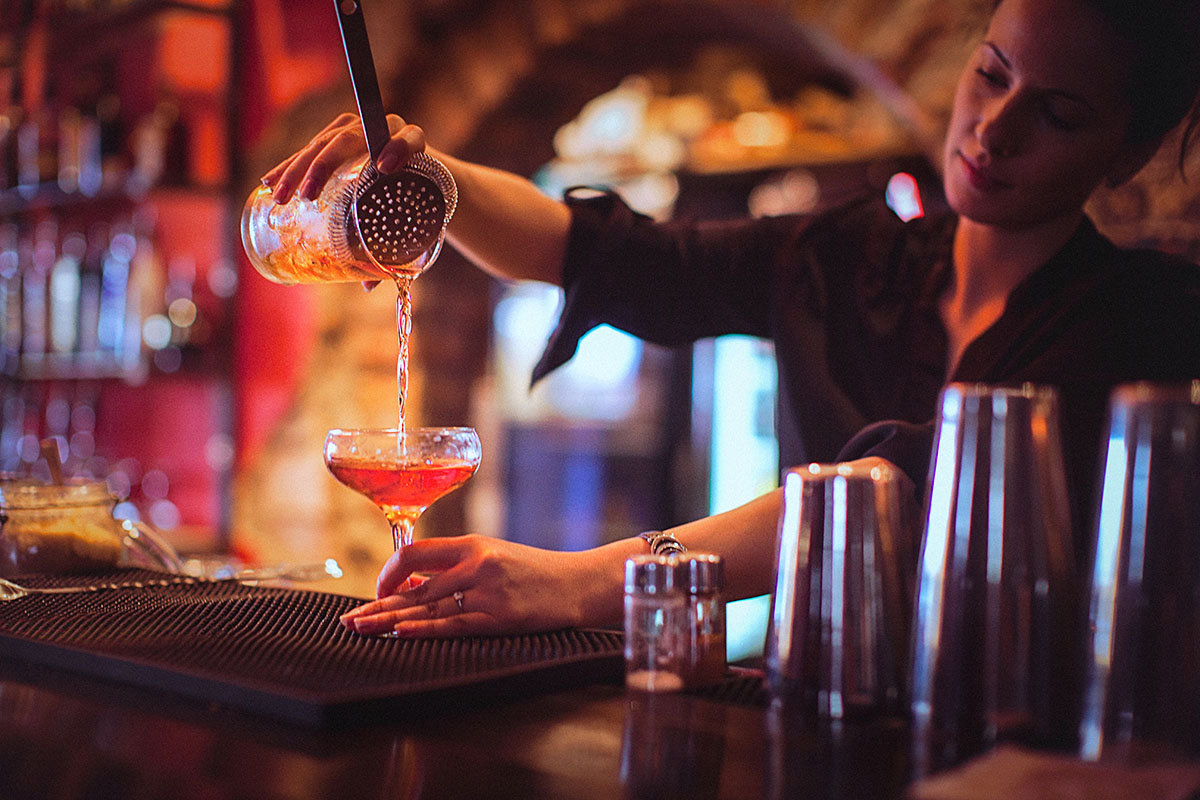 Close-up of a young female bartender pouring cocktail in a nightlife cocktail bar.