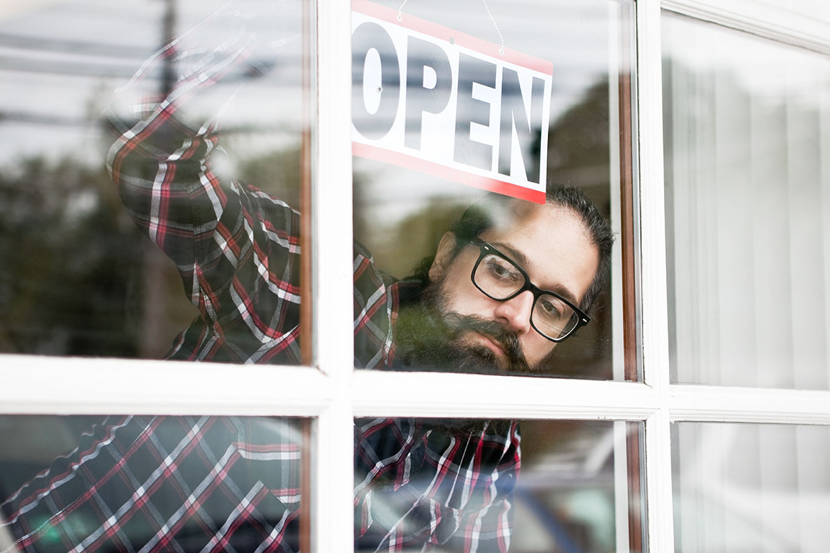 A small business owner hanging an open sign in the window of his business as he looks out seeking customers.