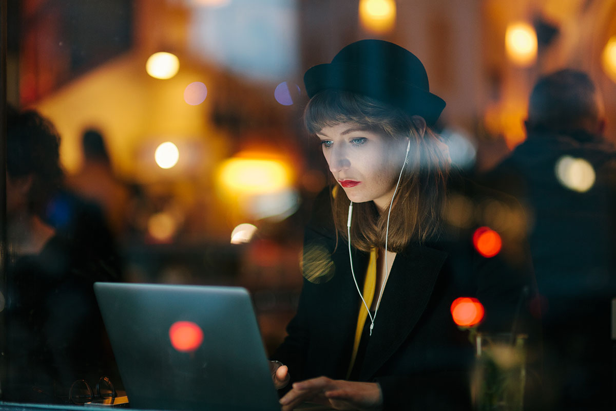 Woman sitting in Cafe and working late at night. She is typing on her Laptop.