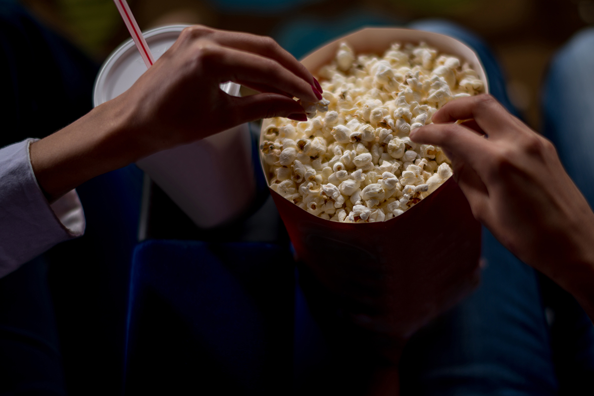 Two people eat popcorn while on a date at the movie theater.
