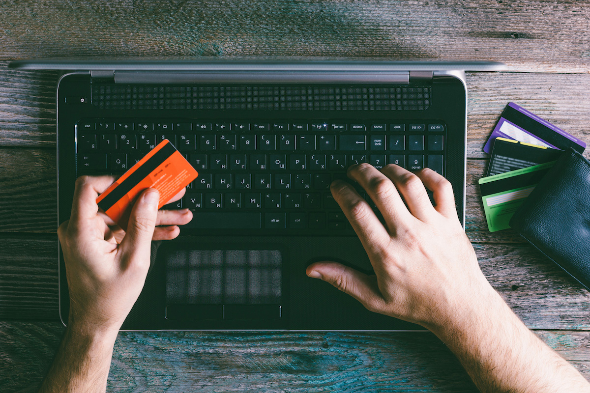 Closeup of a man's hands holding a credit card and using a laptop.
