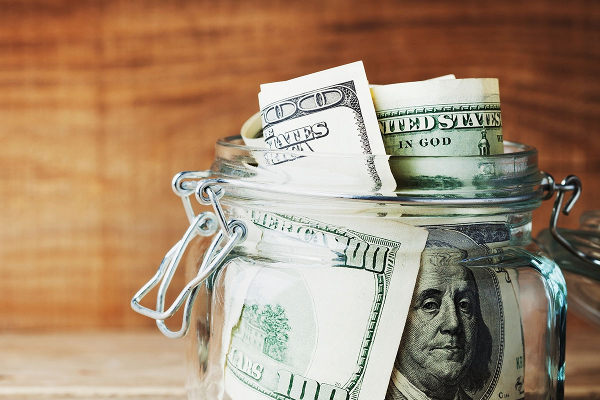 Dollar bills in glass jar on wooden background
