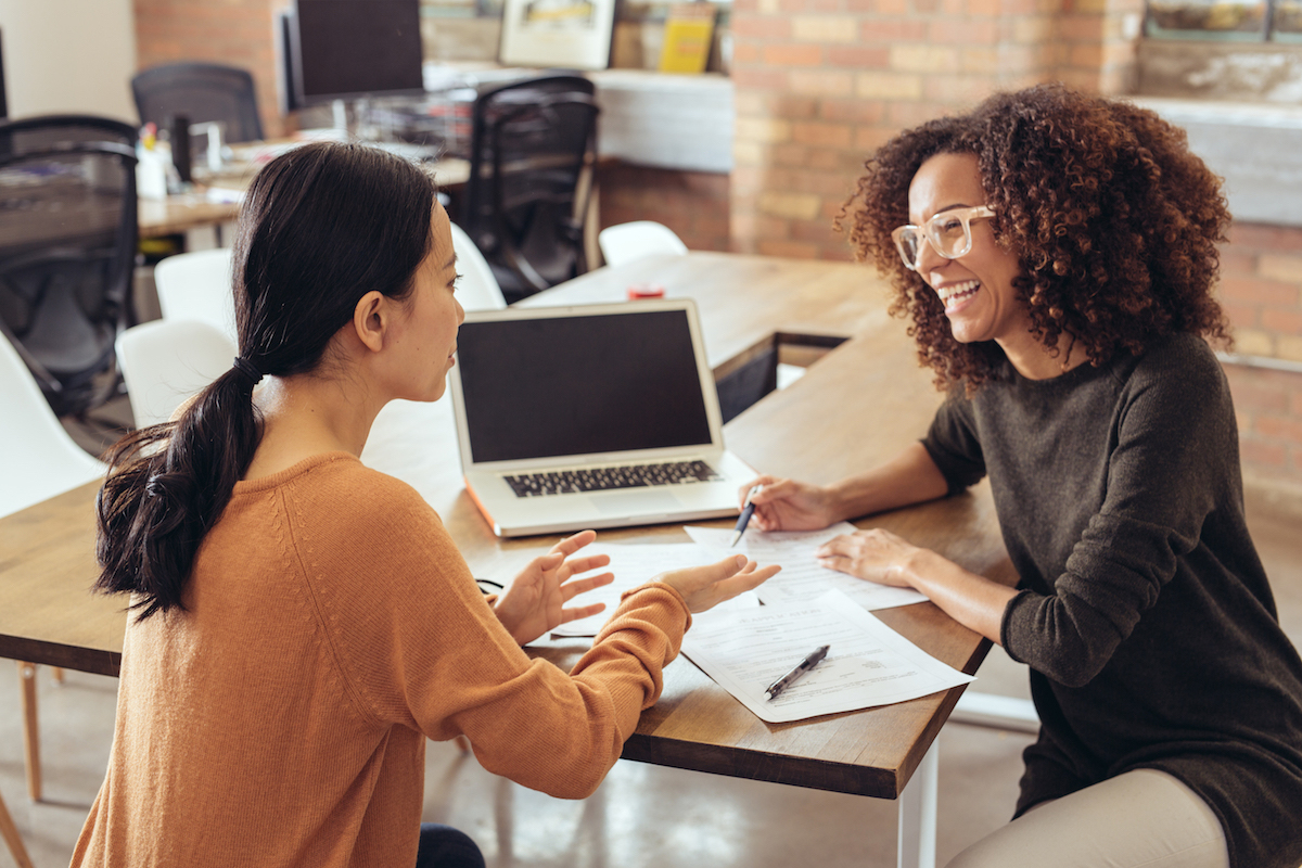 Two women look over financial paperwork with a laptop.