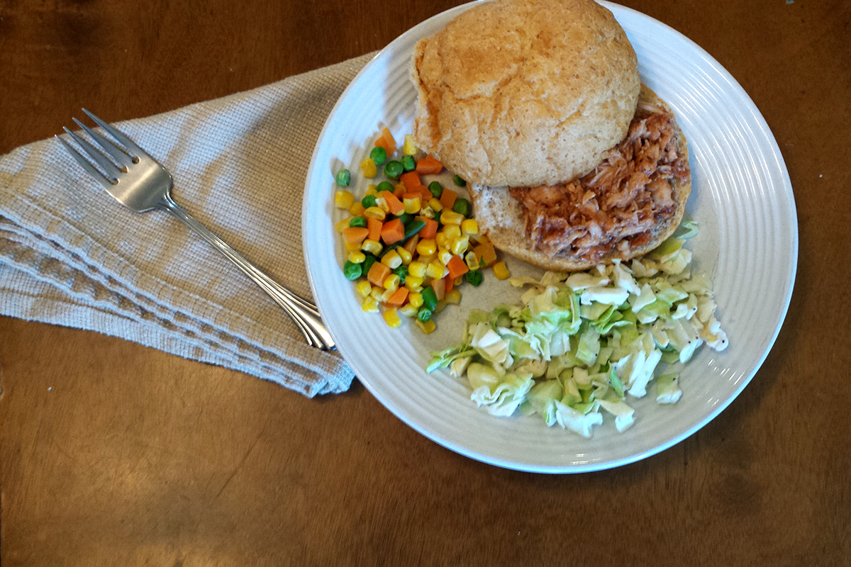a bbq chicken sandwich on a plate with vegetable sides