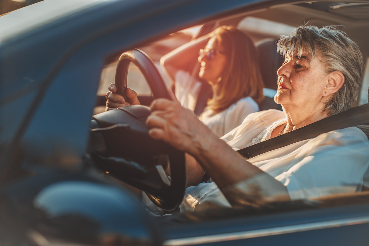 A senior drives a car with a passenger in the passenger seat.