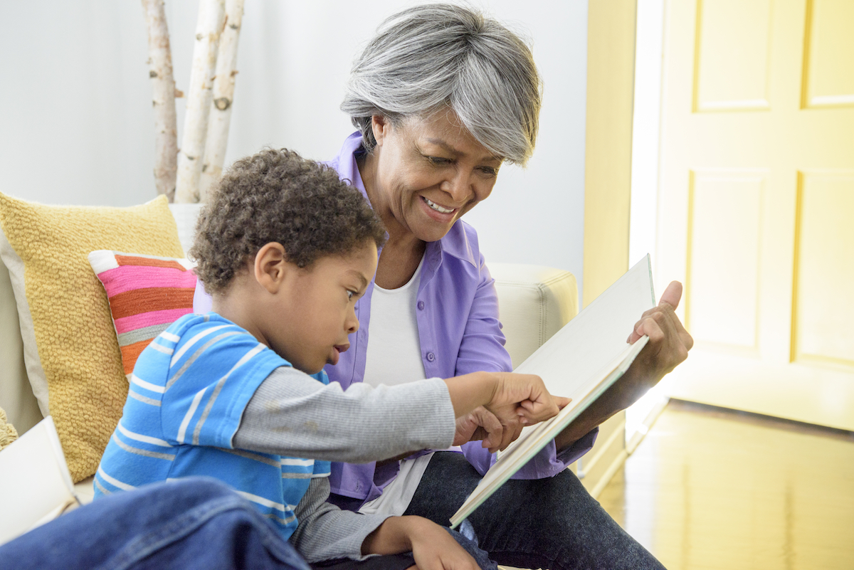 A young boy reads a book with a senior woman.