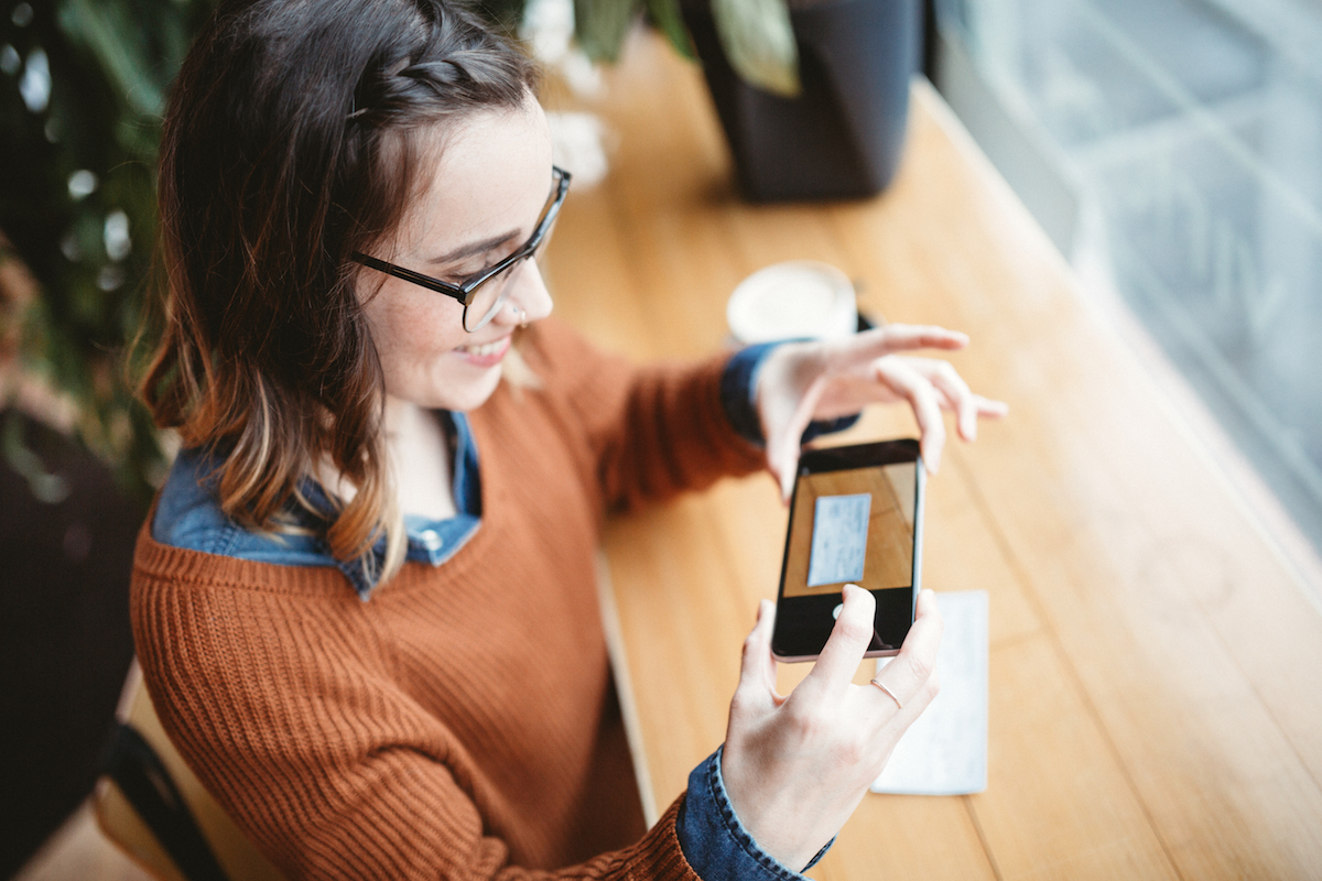 A young woman takes a picture with her smart phone of a check for digital electronic depositing.