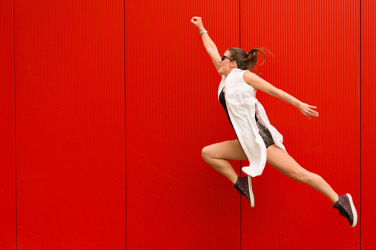Stylish woman dancing and jumping on a street agains a red wall