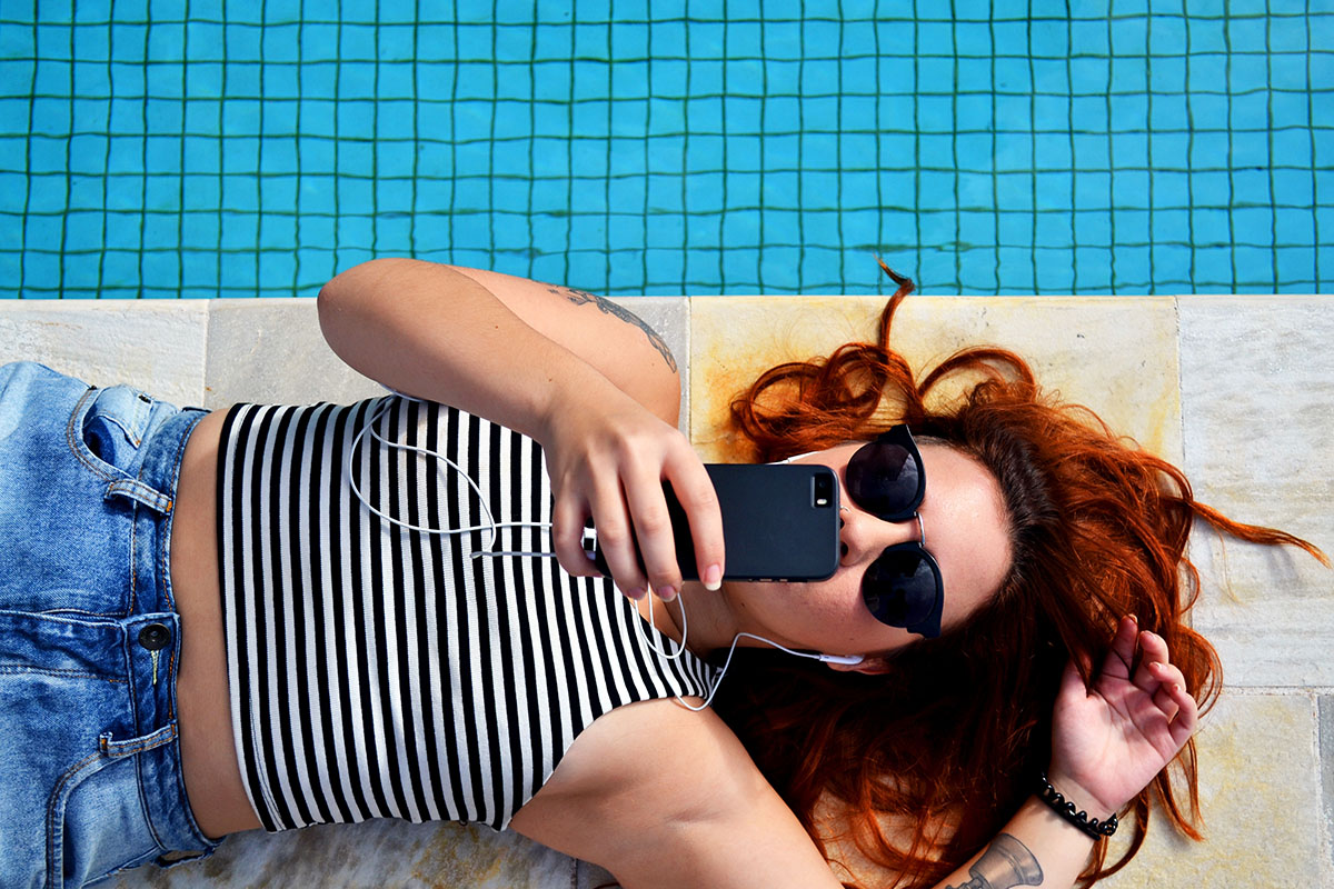 young woman lying by the pool with phone