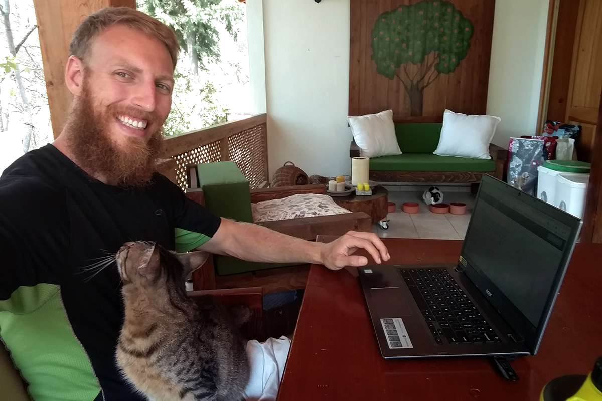 man sitting working on a laptop with a cat in his lap