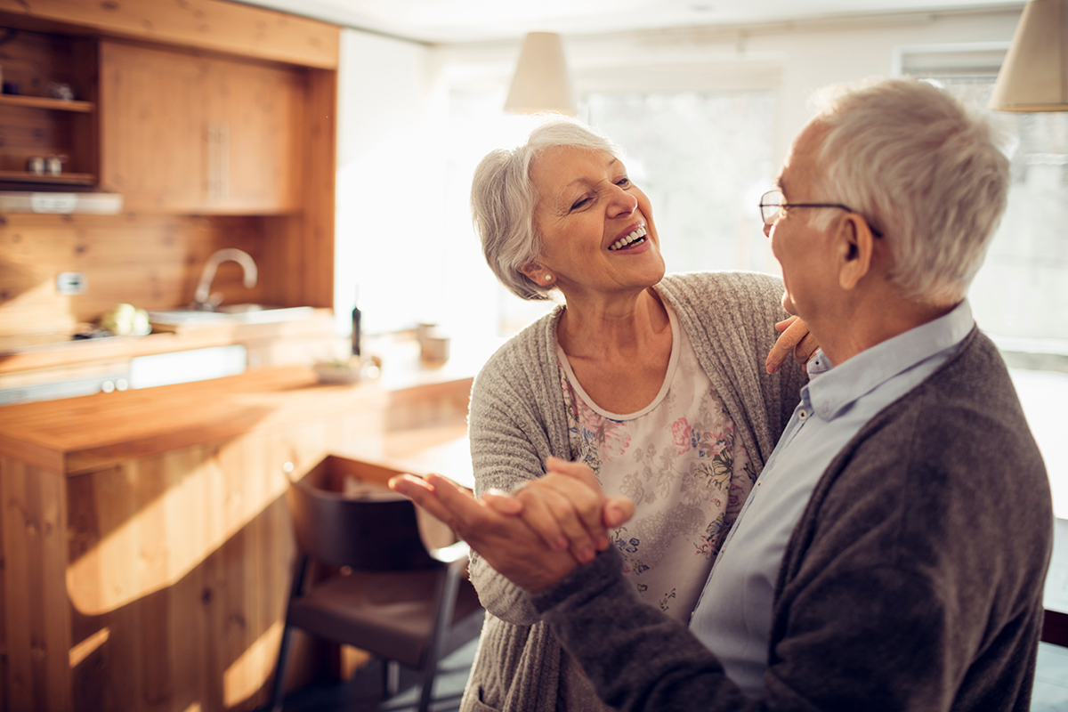 A senior couple dance in the kitchen of their home.
