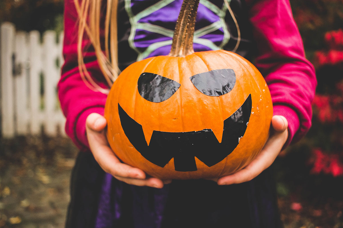 girl in costume holding painted jack-o-lantern