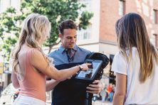 two woman looking at man with tablet outdoors