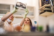 Female dentist examining medical scan of young woman's teeth.