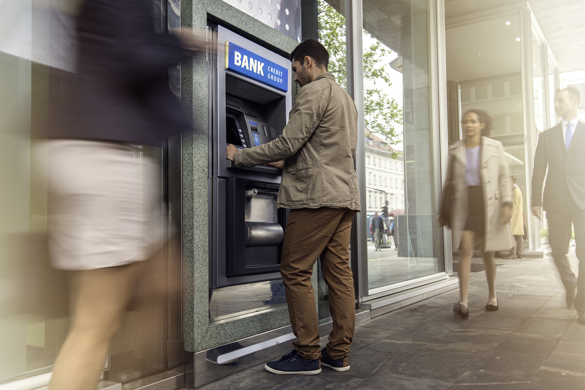 Focus on man standing in front of an ATM machine on a city street