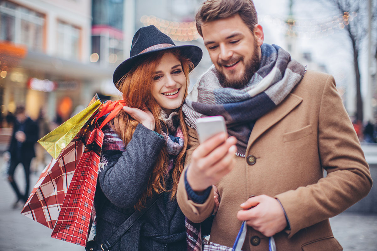 Young couple shopping in downtown. Holding shopping bags and checking smart phone.