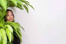 A shy businesswoman hides behind a giant plant at an office.