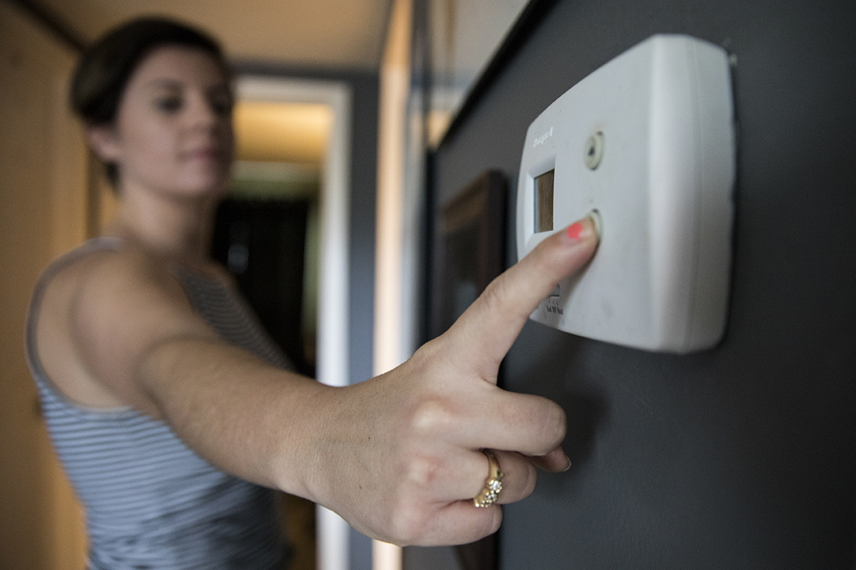 A woman adjusts her thermostat before leaving for vacation