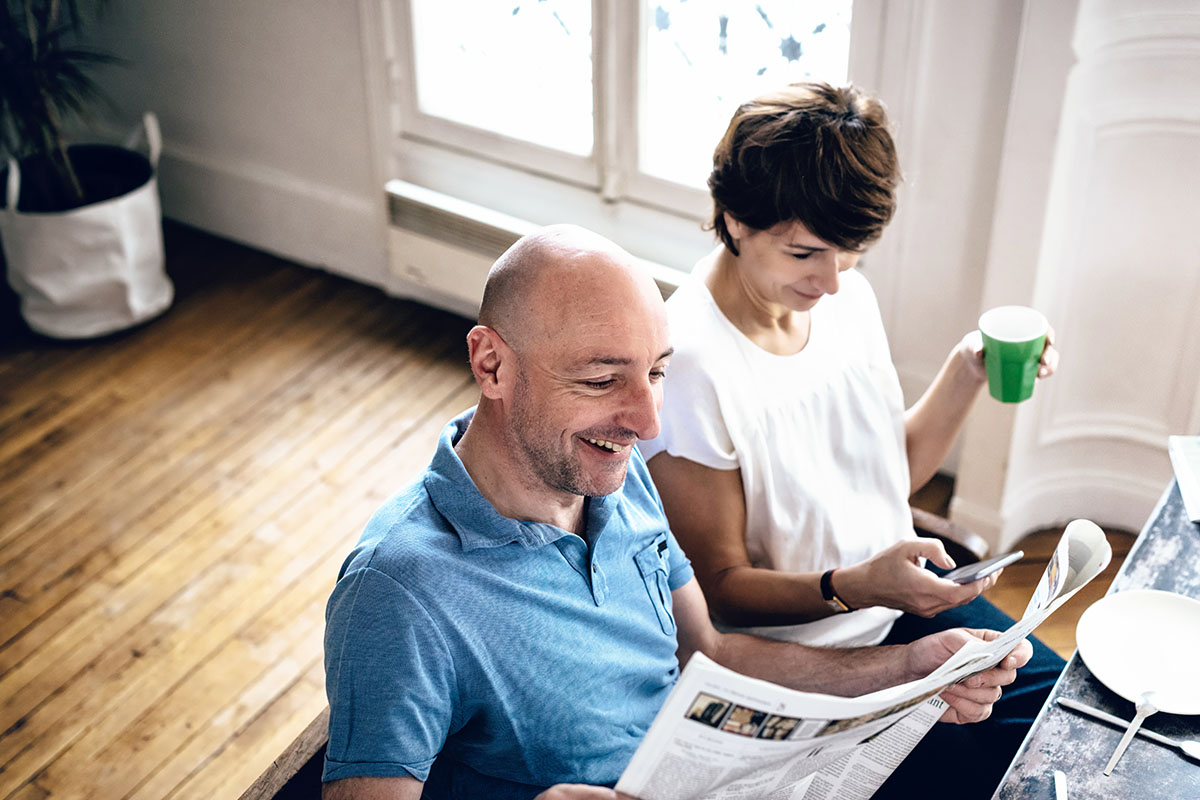 couple reading news in newspaper and on mobile at breakfast table