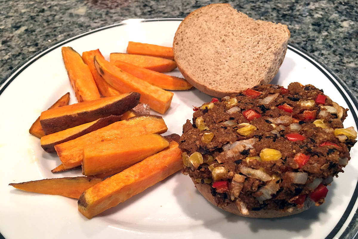 an open faced veggie burger on a plate with sweet potato wedges