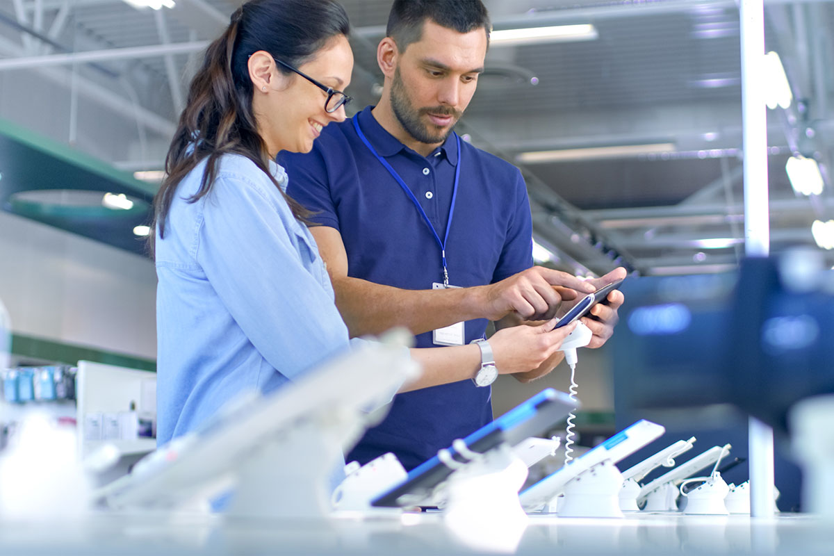 woman looking at tablets in electronics store with the help of male employee