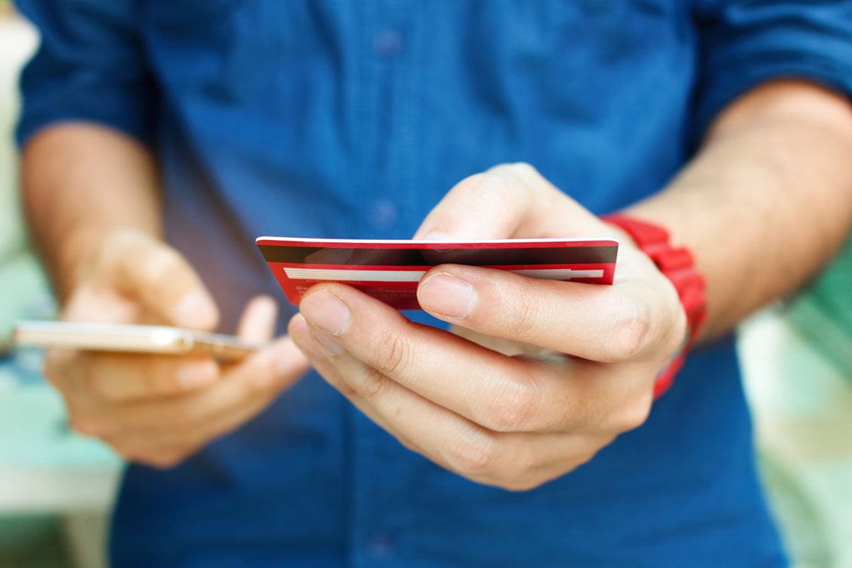 Close up man holding credit card while using smartphone.