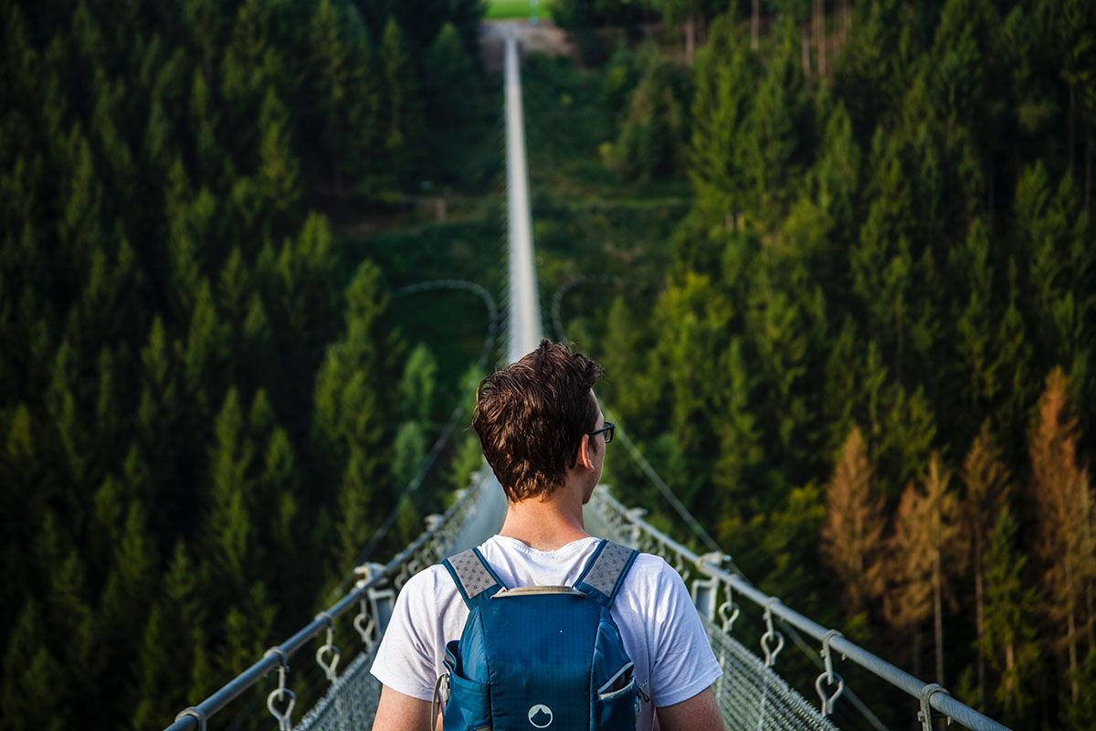 young man hiking on a long suspended bridge