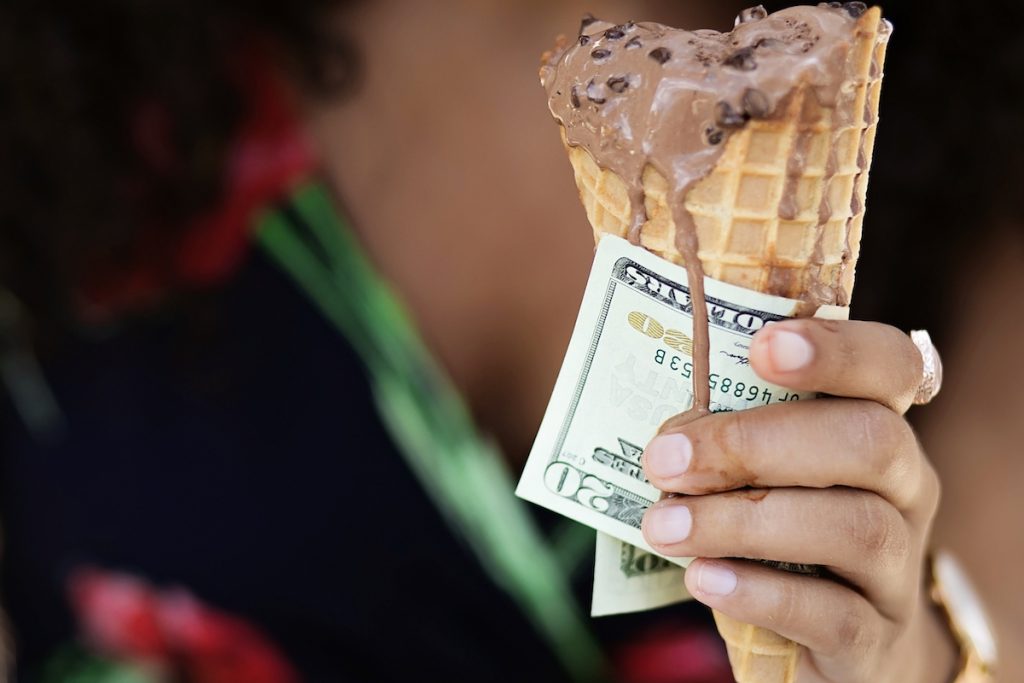 A woman holds a dripping ice cream cone and a $20 bill.