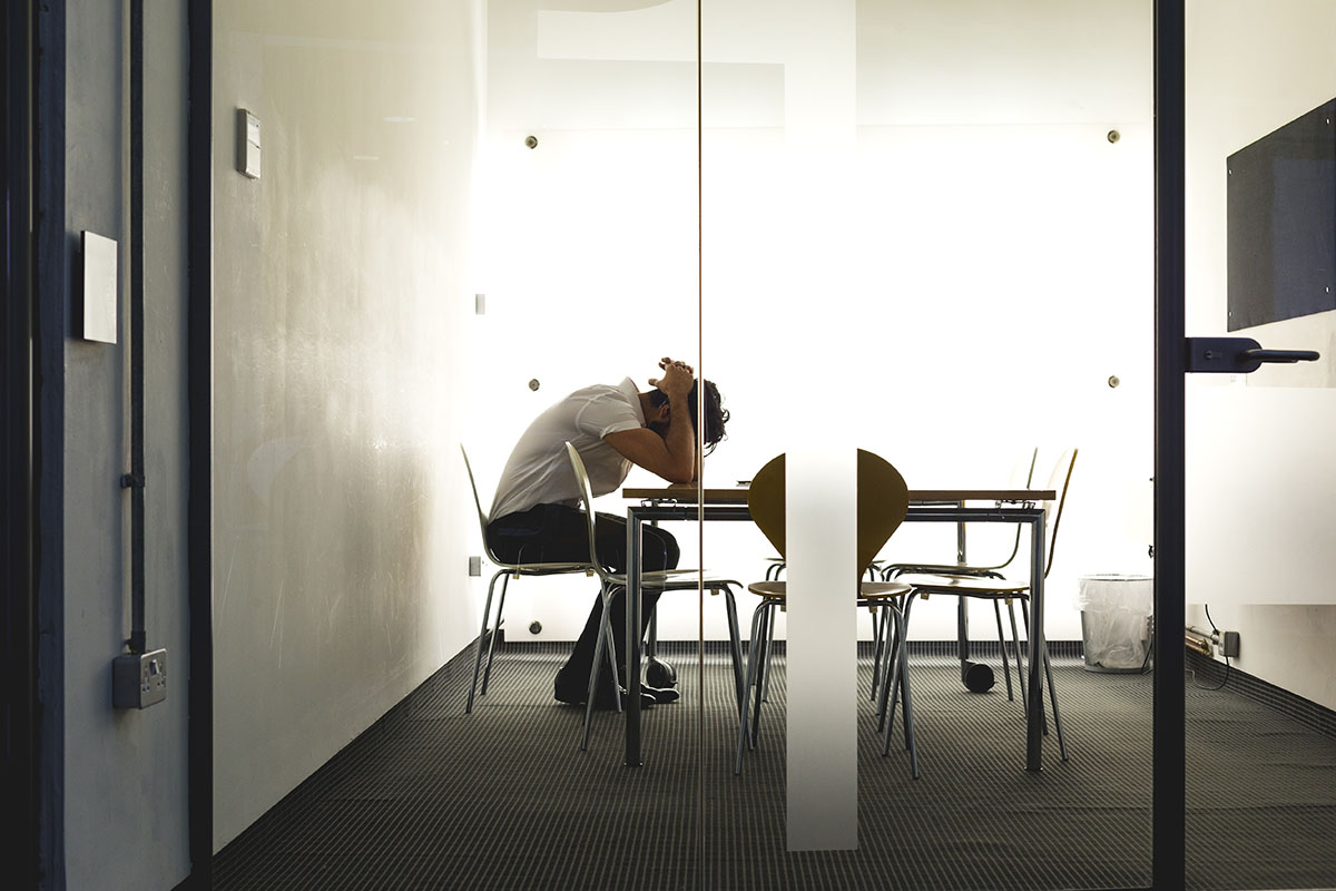 Businessman sits with his head in his hands leaning forward over a table.