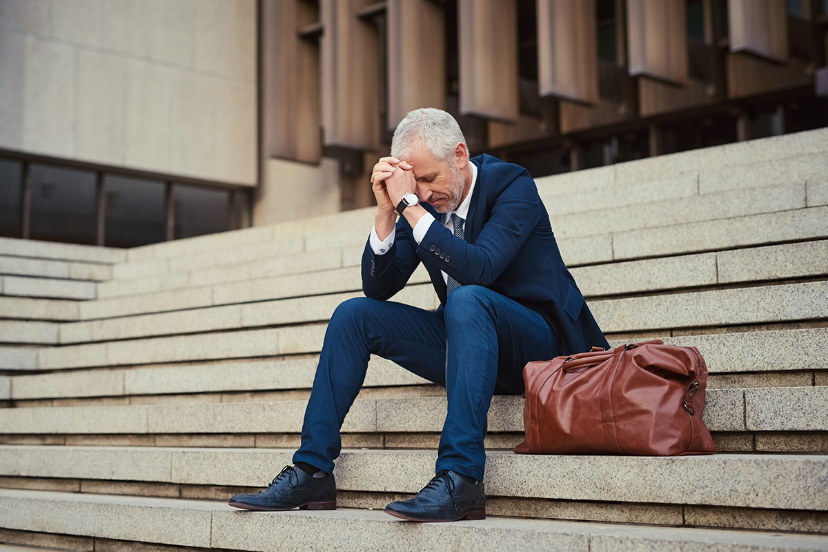 Shot of a dejected businessman sitting on the stairs outside his office with his head in his hands