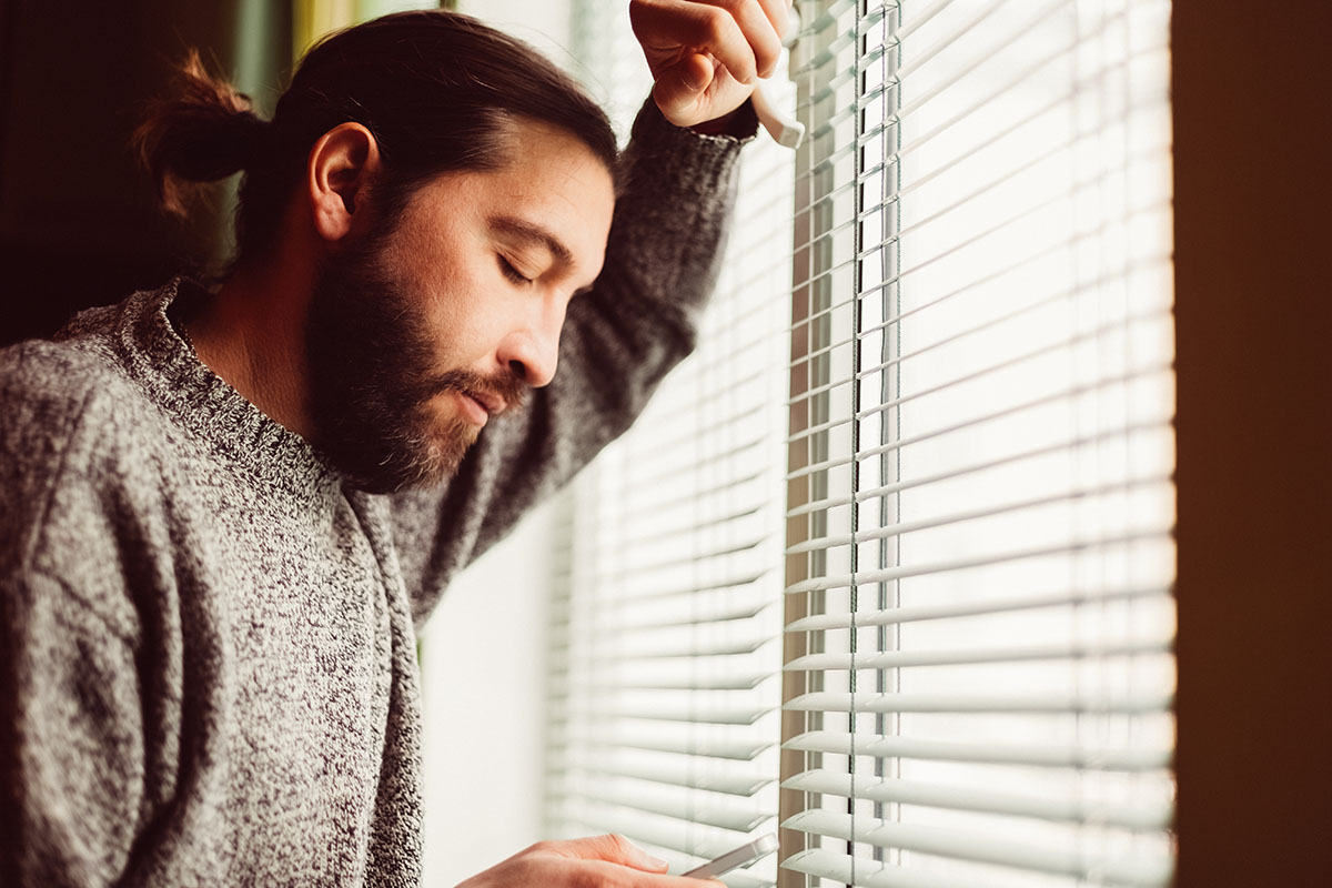 man standing by window looking down at phone
