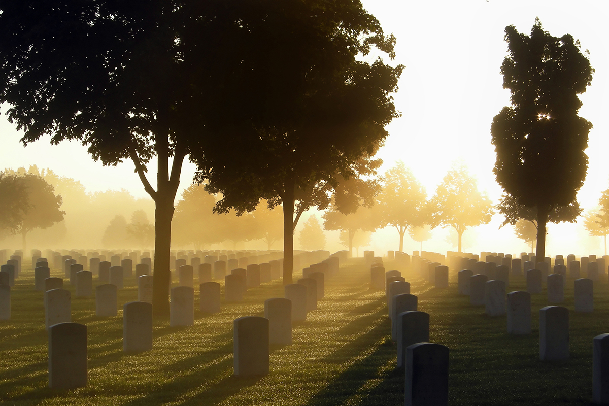 A cemetery surrounded by trees as the sun rises in the morning.