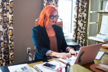 A young woman with bright red hair works from home on her laptop.