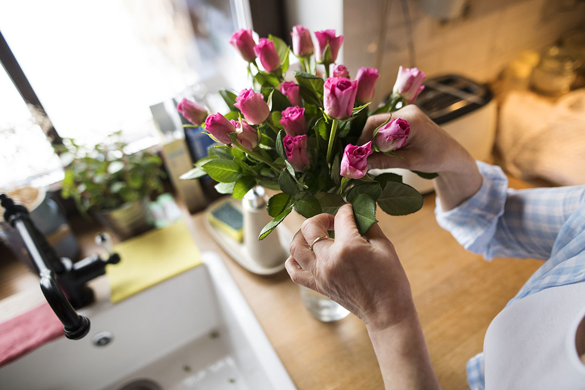 woman at home in her kitchen arranging roses in vase