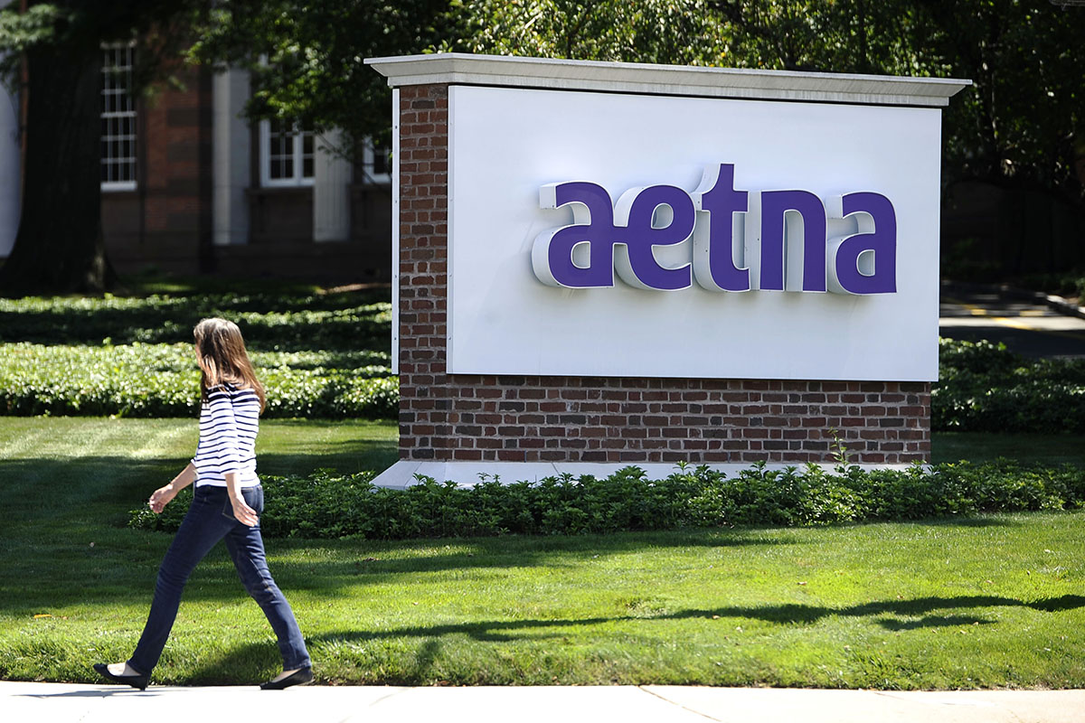 A pedestrian walks past a sign for health insurer Aetna Inc., at the company headquarters in Hartford, Conn.