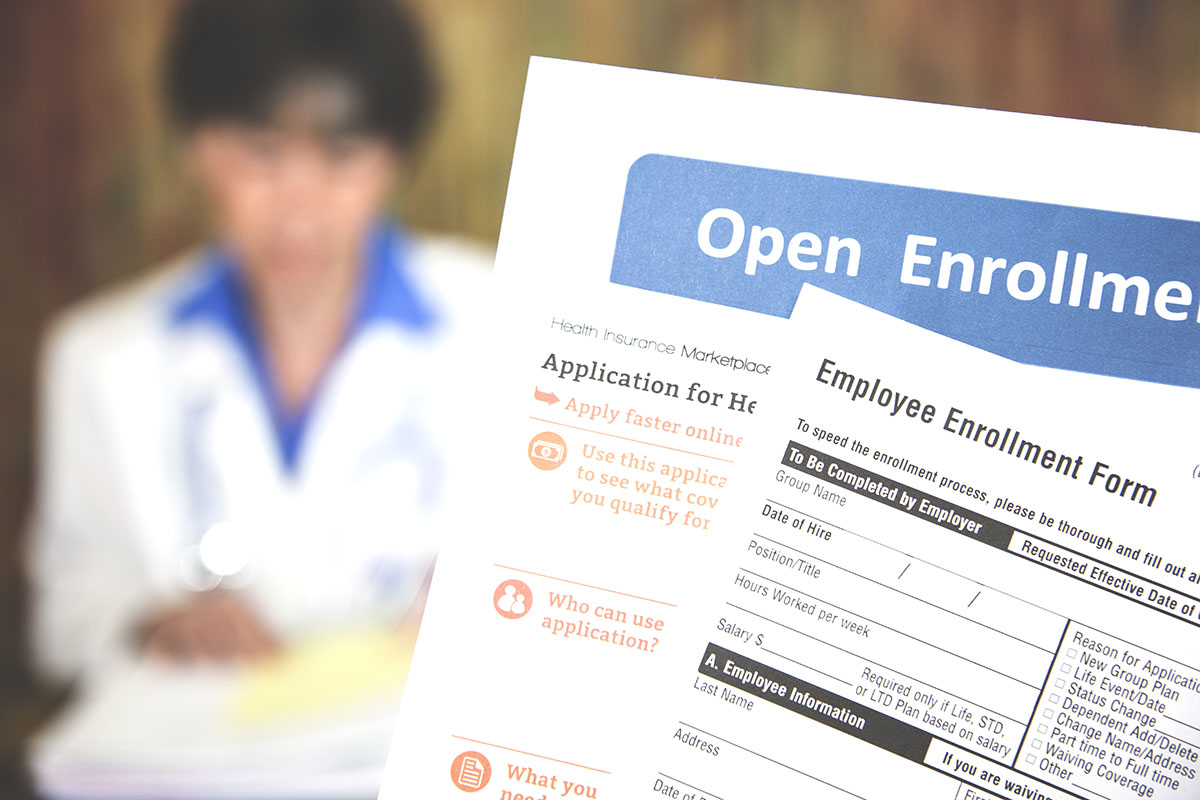 Patient holding open enrollment healthcare benefits forms with a medical doctor in the background.
