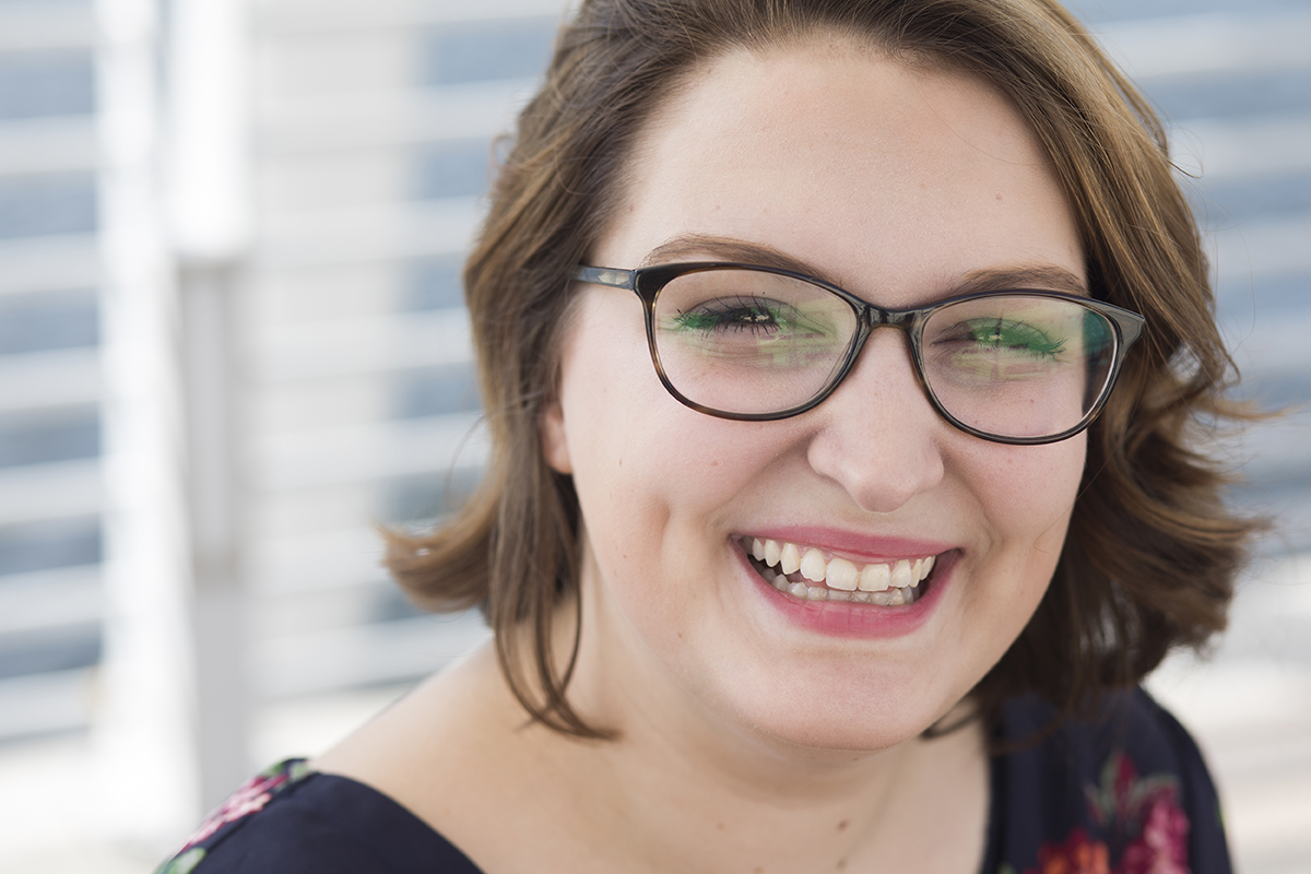 A young woman wearing glasses smiles for the camera.