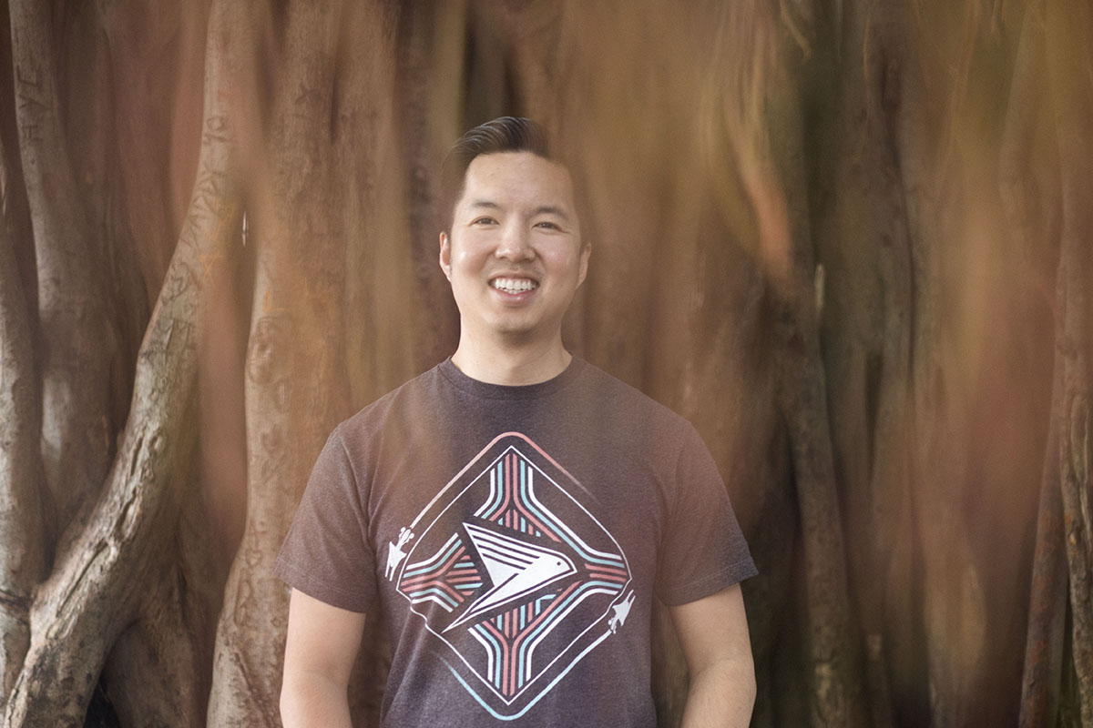 A young man smiles for the camera as he is surrounded by a large tree.