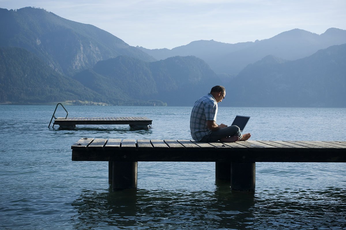 Man on a jetty working outdoors on laptop
